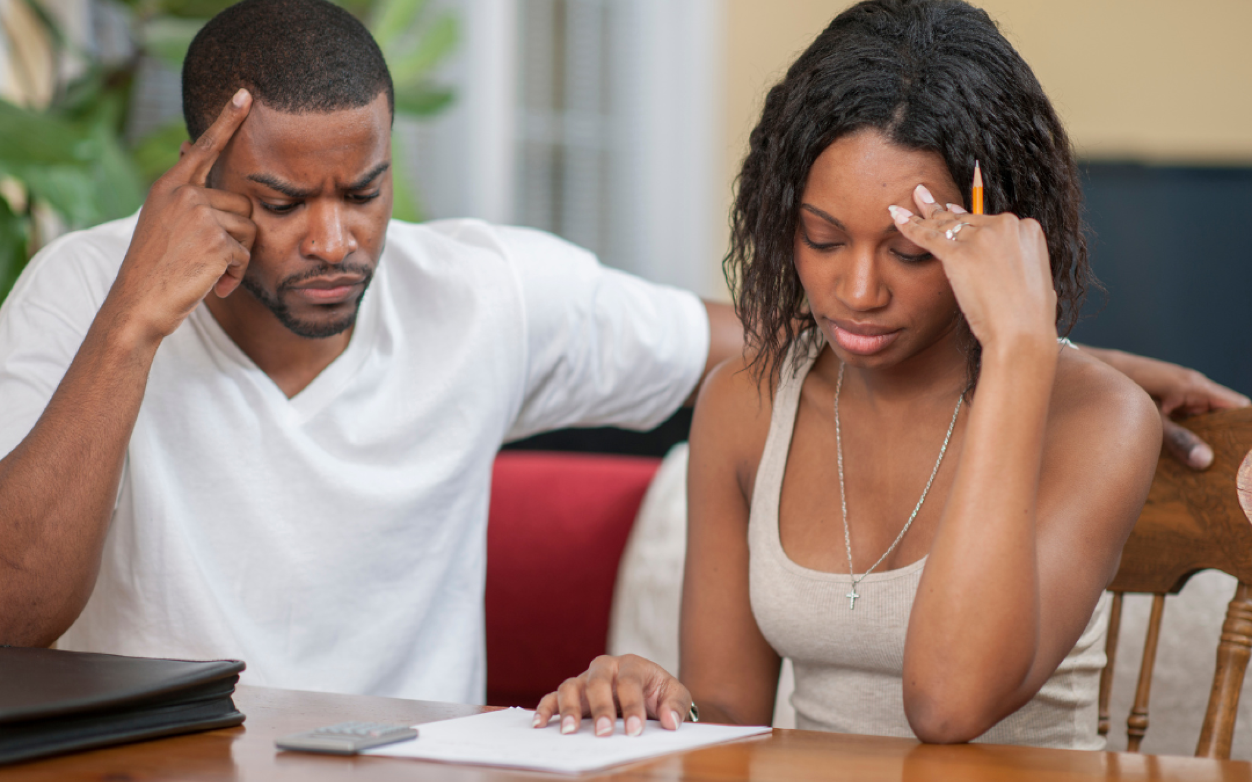 A man and a woman sit with their hands to their temples reviewing financial information.