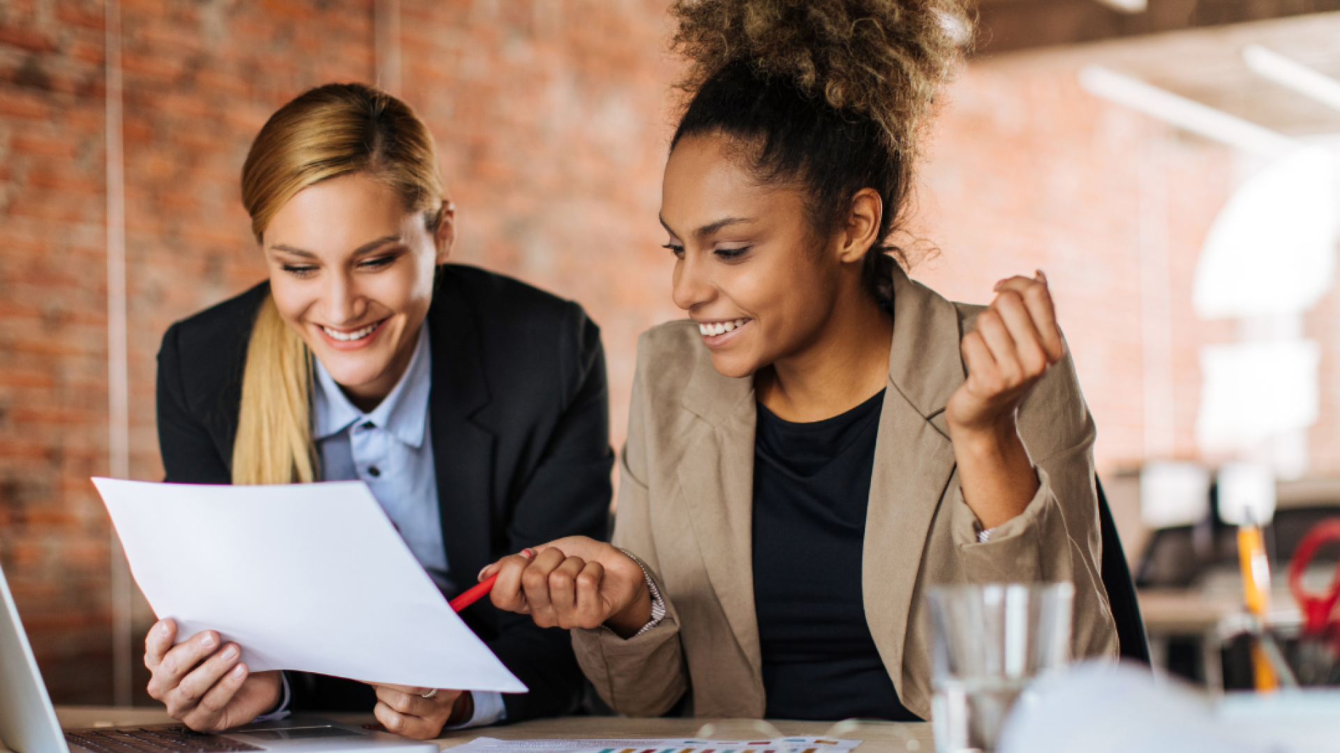 Two women collaborate at work in front of a piece of paper and a laptop