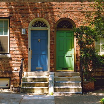 Photo of two rowhomes. One door is painted bright green and one is painted bright blue.  Photo by Tyler Finck on Unsplash