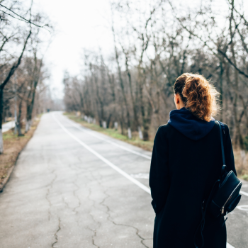 A woman stares down a long and empty road